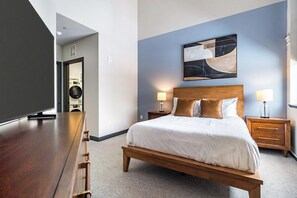 Une chambre d’hôtel moderne avec un grand lit, une tête de lit en bois, deux tables de chevet avec des lampes, un téléviseur à écran plat et un tableau au mur.