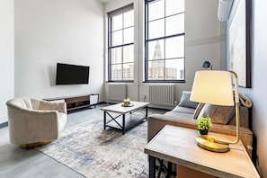 A modern living room with a sofa, armchair, coffee table, and a TV mounted on the wall. - Landing | Beautiful 1BD in Downtown Hartford (Hartford)