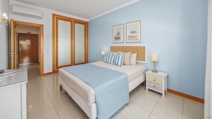 A hotel room with a bed, bedside tables, a wardrobe, and an air conditioning unit. - Super Beach Apartment w/ Pool in the private condominium of Quinta da Barracuda (Albufeira)