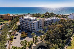 Ein mehrstöckiges Hotel mit Balkonen, die auf einen Strand und das Meer blicken.