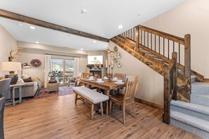 A spacious living room with a wooden dining table, comfortable seating, a staircase, and a fireplace. - Timberline Hideaway with Hot Tub (Hollister)