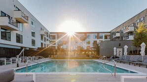 Un área de piscina moderna con vista despejada, sillas de descanso y un edificio con balcones.