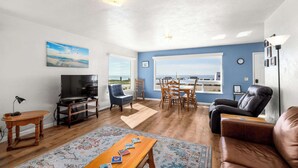Sala de estar com televisão, sofá de couro, mesa de jantar, cadeiras e vista para o mar.