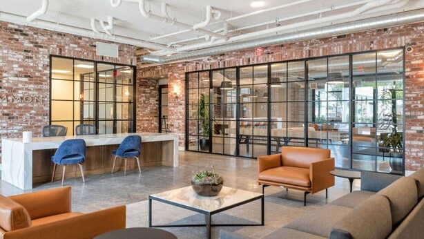 Een moderne lounge met een metselwerk muur, een receptiebalie, zithoeken en grote ramen.