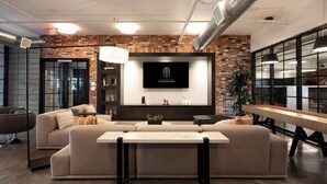 Een moderne woonkamer met een grote hoekbank, een flatscreen televisie bevestigd aan een bakstenen muur en een lange houten tafel.