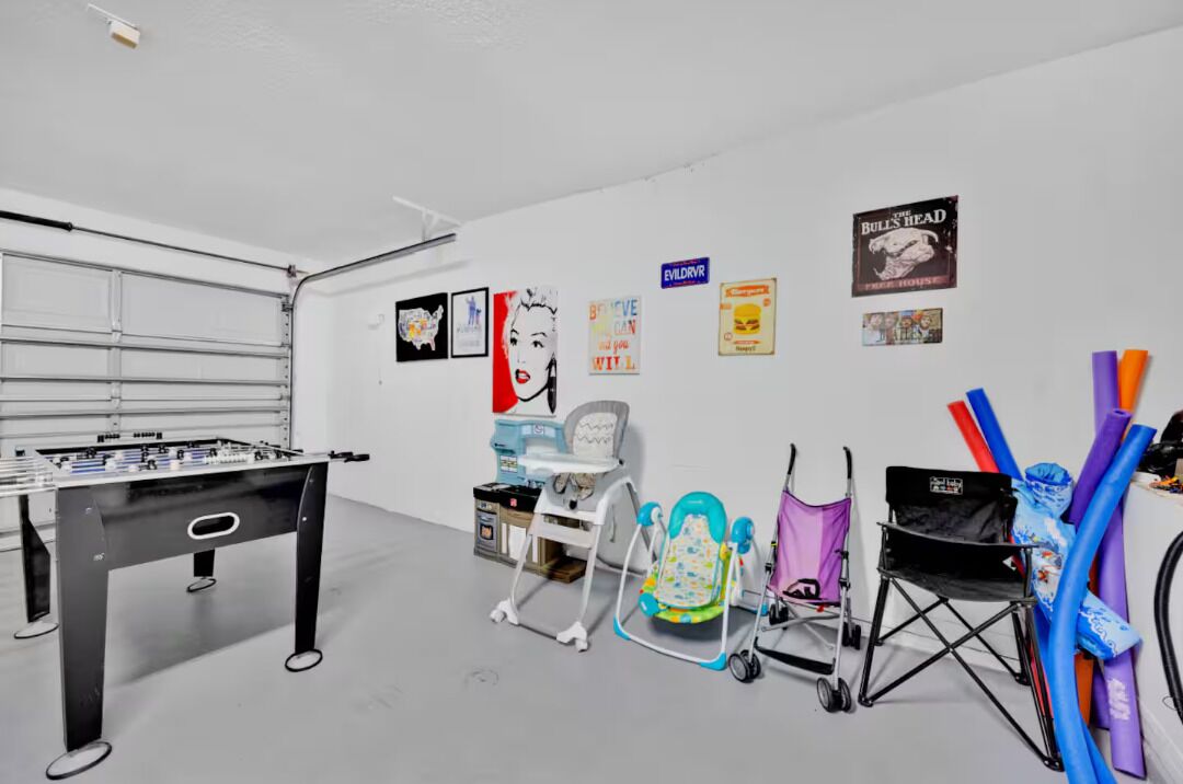 A room with a foosball table, a baby walker, a high chair, and various colorful items on the wall.