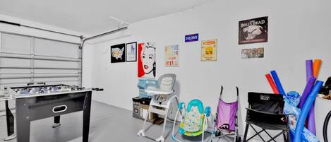 A room with a foosball table, a baby walker, a high chair, and various colorful items on the wall.