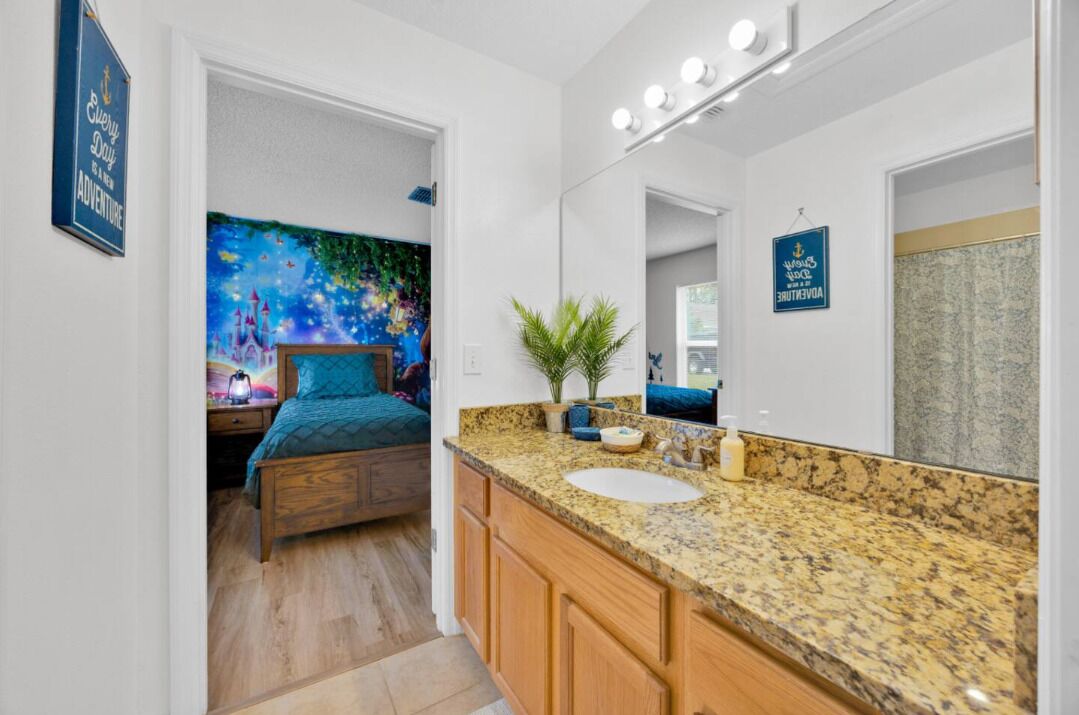 A bathroom with a granite countertop, a sink, and a mirror. There is a painting on the wall and a sign above the mirror.