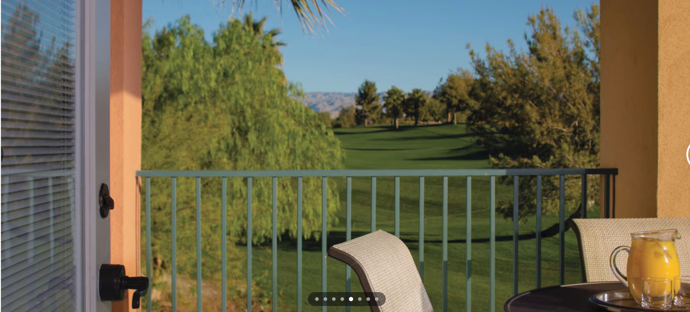 Un balcón con vistas a un campo de golf, una mesa con una jarrón y vasos, y una silla.