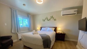A neatly arranged bedroom with a large bed, bedside lamps, a heater, and an air conditioning unit. - Cozy Bayfield Retreat • Pool & Hot Tub • Near Grand Bend • Lake Huron Nearby 2 (Bayfield)