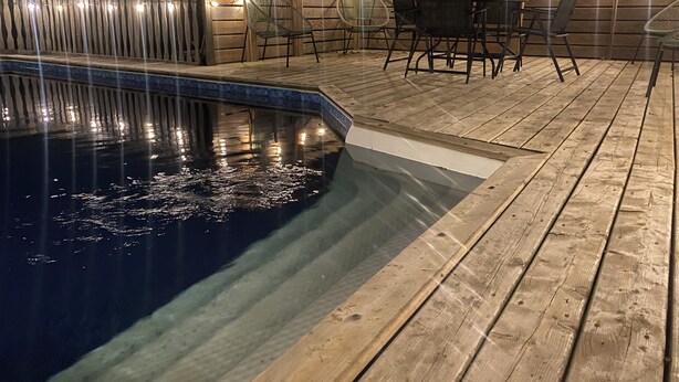 A wooden deck with a pool, surrounded by chairs and tables, and string lights. - Cozy Bayfield Retreat • Pool & Hot Tub • Near Grand Bend • Lake Huron Nearby 2 (Bayfield)