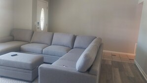 Un sofá modular con un reposapiés a juego en una habitación con paredes de colores claros y suelo de baldosas.