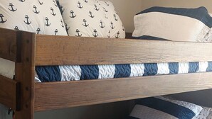 Una cama litera con colchón azul y blanco a rayas, estructura de madera y almohadas a juego con estampados de anclas.