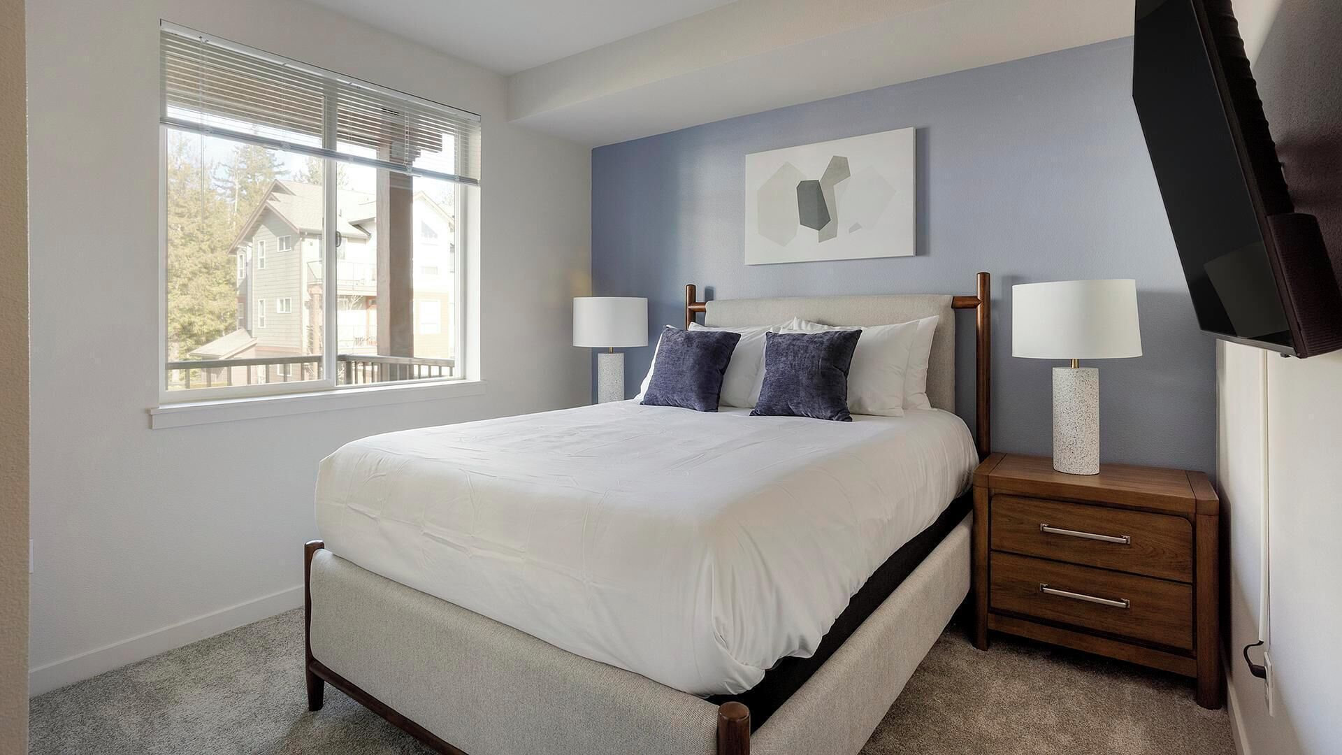 Une chambre à coucher comprenant un lit, deux tables de chevet, une fenêtre et un téléviseur fixé au mur.