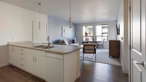 A modern kitchen with a central island, a dining area with a table and chairs, and a living space with a sofa and a TV. - Landing | Amazing 1BD, Clubhouse, Pool (Marysville)