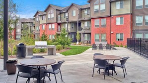Un patio con mobiliario exterior, una parrilla y un pequeño jardín.