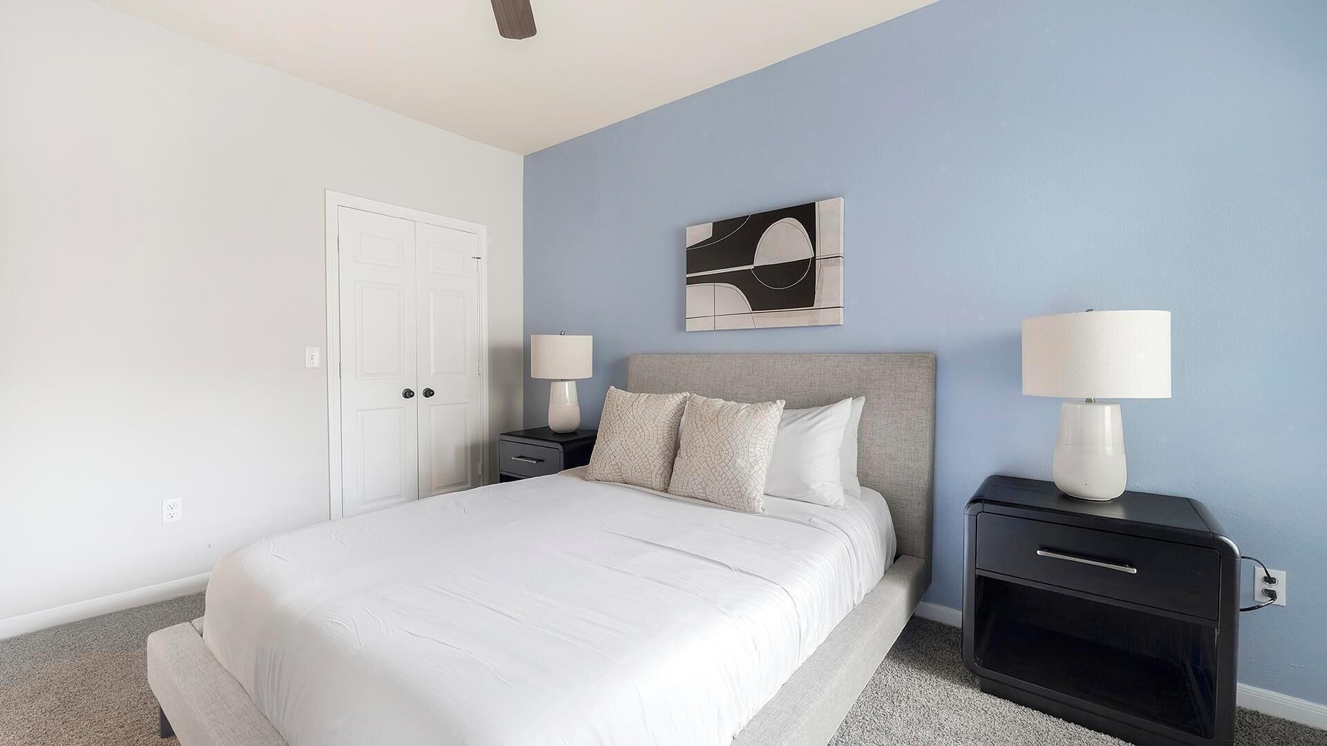 A hotel room with a bed, two bedside tables with lamps, a wall-mounted artwork, and a door.