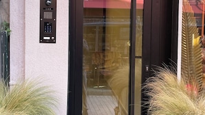 Ingresso di un edificio con porta in vetro, tastierino per la sicurezza e un cartello che recita 'MAISON7'.