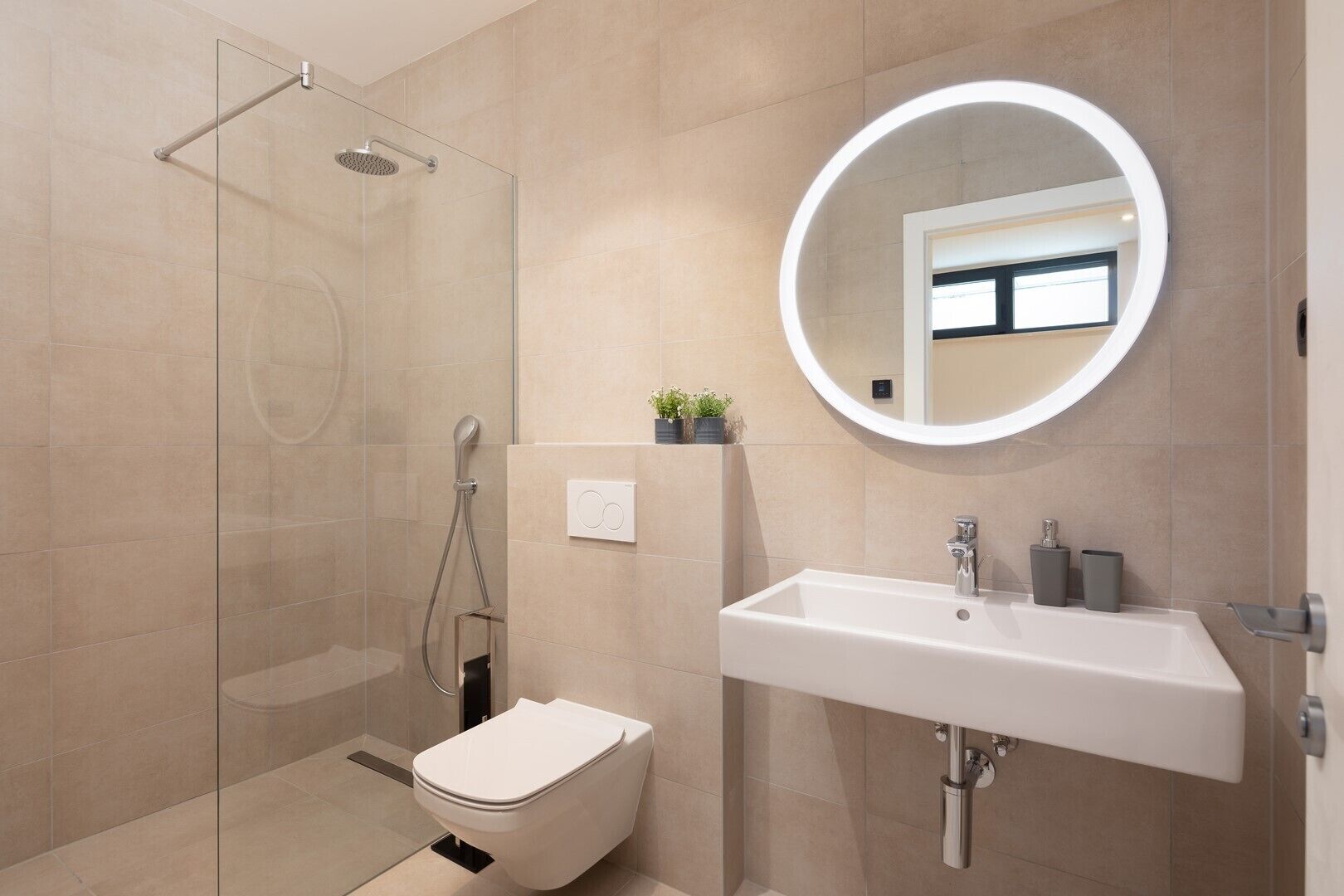 Un baño moderno con cabina de ducha de vidrio, inodoro, lavamanos con espejo y una planta pequeña en la pared.
