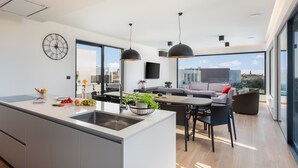 Eine moderne Küche mit einer großen Kochinsel, ein Essbereich mit Tisch und Stühlen und ein Wohnbereich mit einer Couch und Blick auf die Stadt.