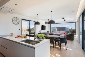 Eine moderne Küche mit einer großen Kochinsel, ein Essbereich mit Tisch und Stühlen und ein Wohnbereich mit einer Couch und Blick auf die Stadt.