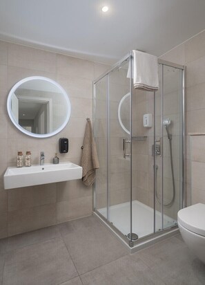 Un baño moderno con cabina de ducha de vidrio, un lavamanos blanco con espejo y un inodoro.