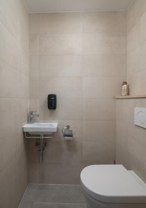 Un baño pequeño y moderno con inodoro, lavamanos y secamanos.