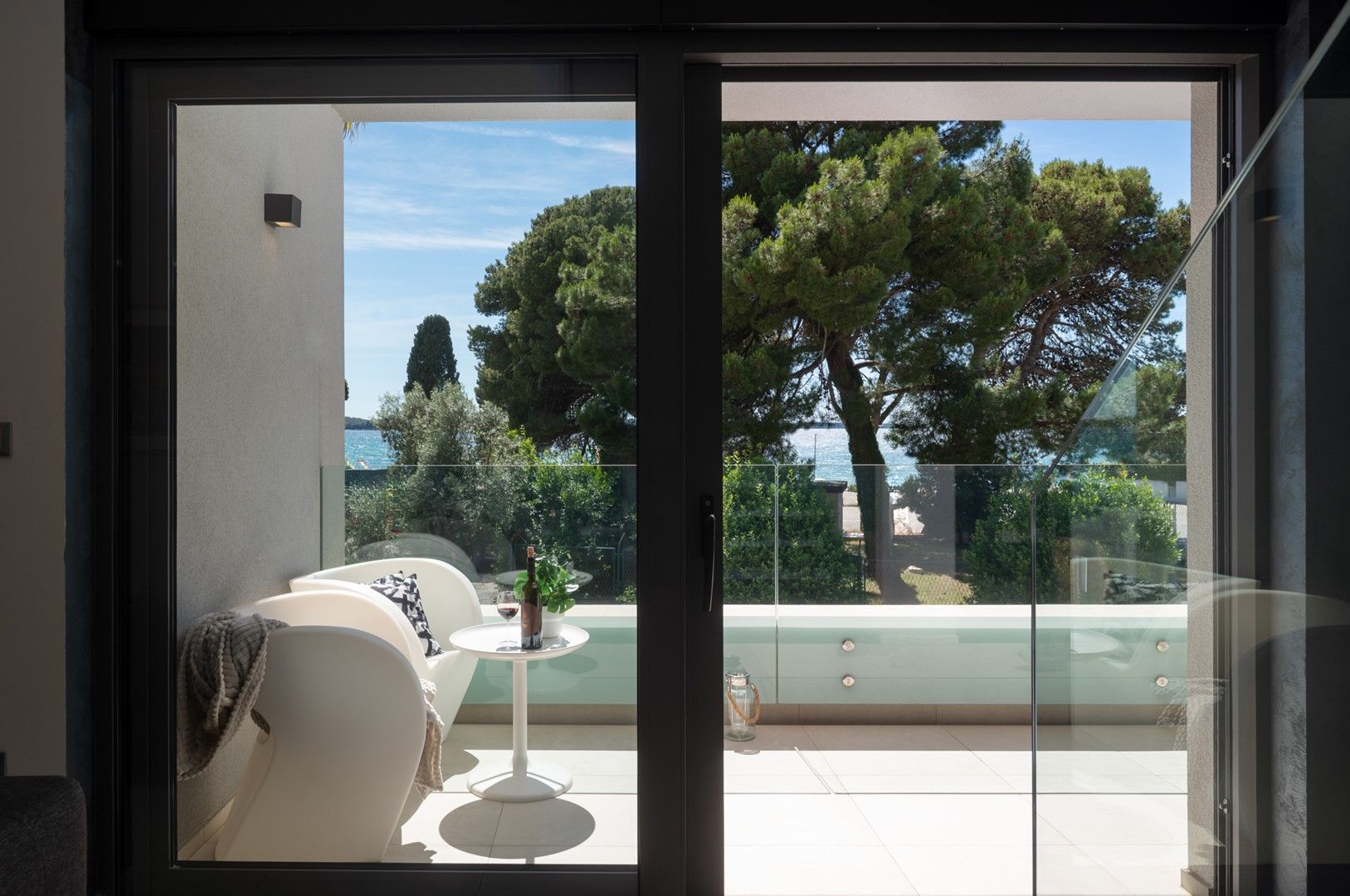Een moderne woonkamer met een glazen deur die leidt naar een balkon met uitzicht op bomen en een wateroppervlak.