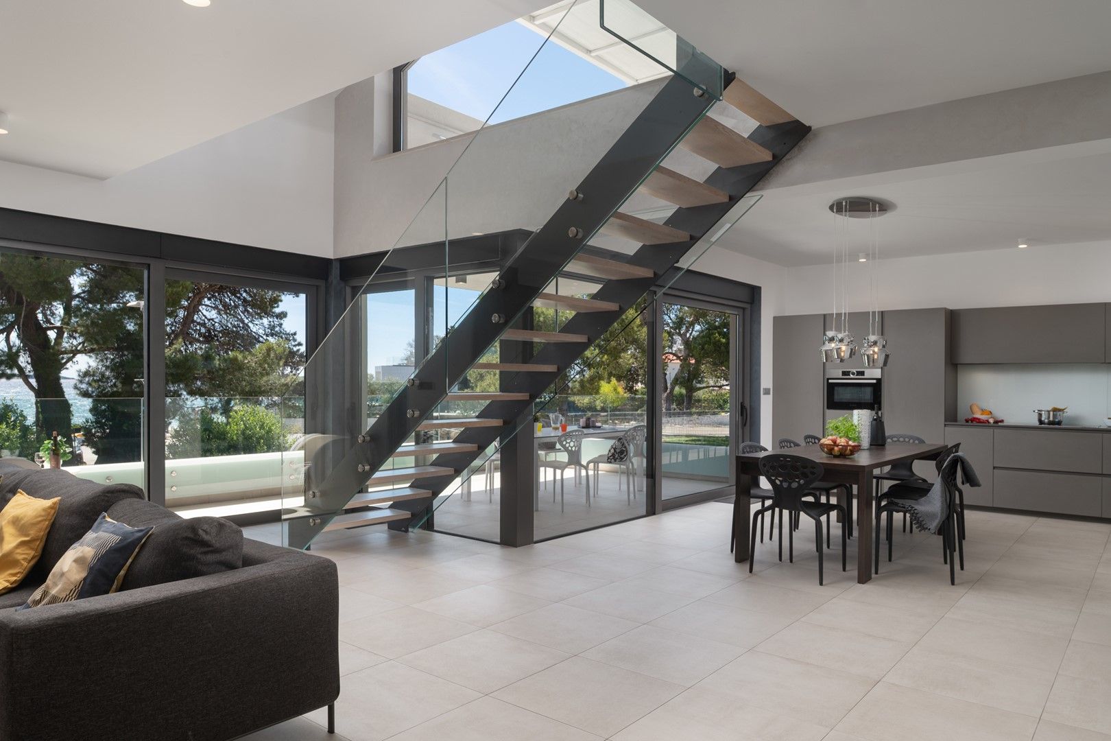 A modern interior with a staircase, dining area, kitchen, and large glass doors leading to a pool.