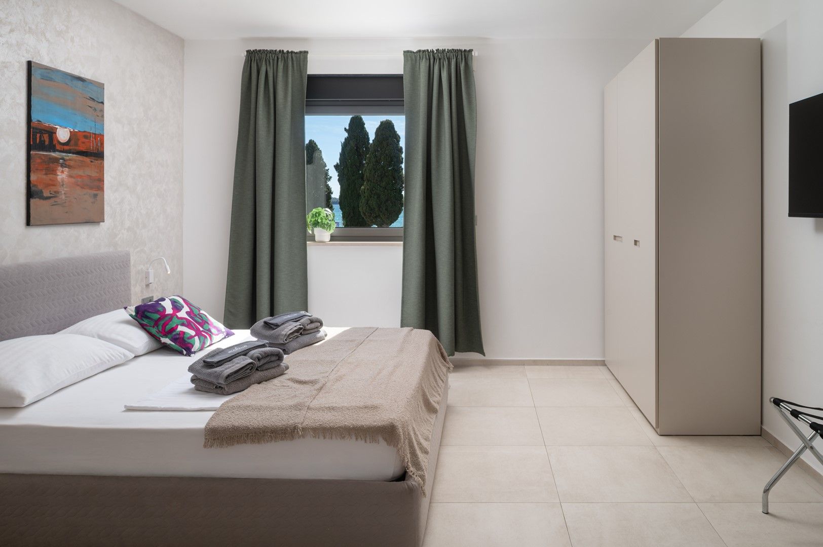 Une chambre à coucher avec un lit, une fenêtre avec des rideaux, un tableau au mur et une armoire.