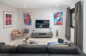 Ein modernes Wohnzimmer mit einem grauen Sofa, einem Fernseher, abstrakter Kunst und einer grauen Ablage.