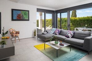 Una sala de estar moderna con un sofá gris, almohadones coloridos, una mesa de centro y un amplio ventanal con vistas a la vegetación.