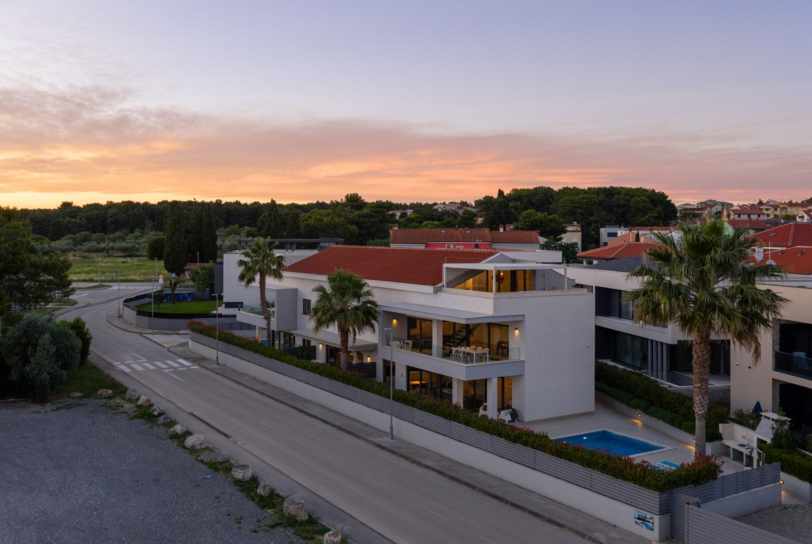 Un edificio residencial moderno con piscina, rodeado de vegetación y una carretera curva.