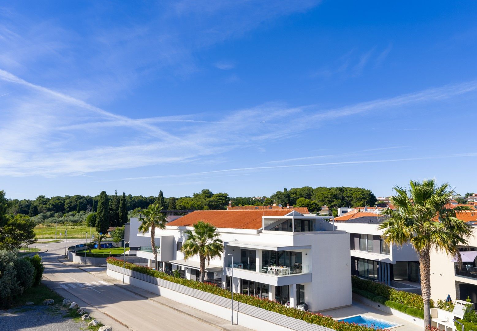A modern residential building with a swimming pool, surrounded by greenery and a clear sky.