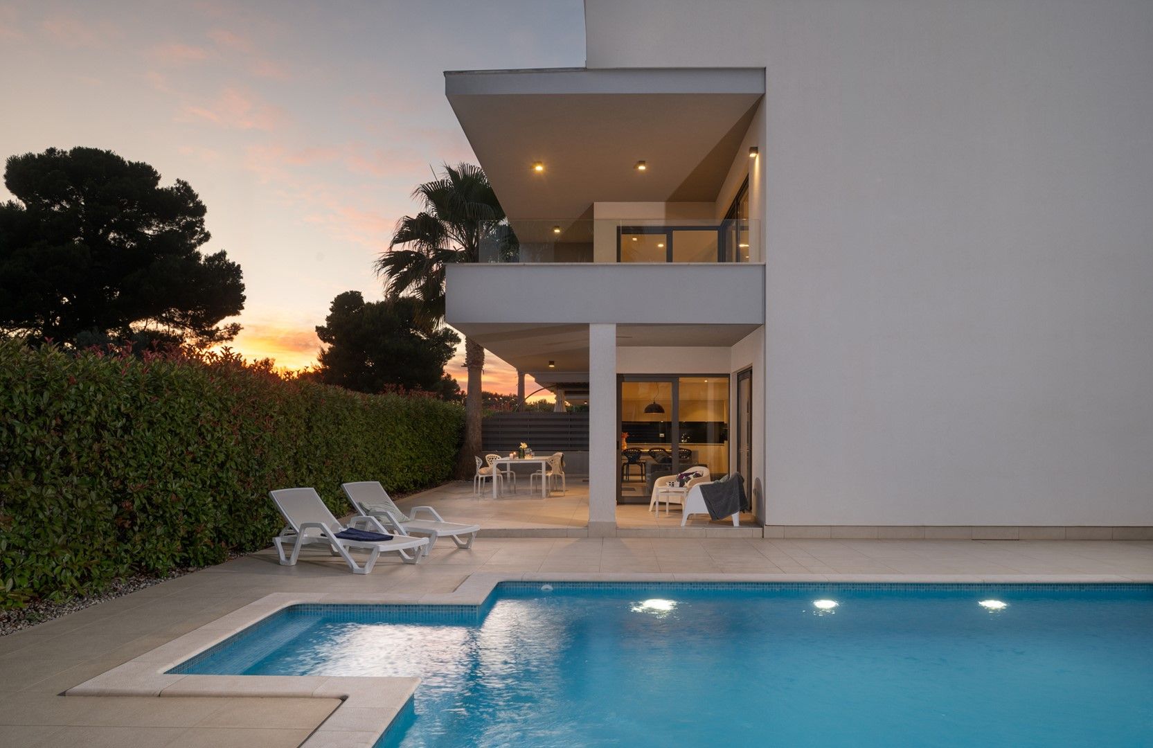 A modern two-story house with a swimming pool, outdoor seating, and a view of the sunset.