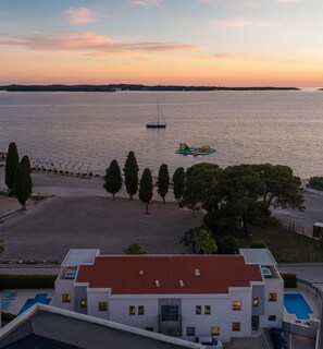 A modern building with a red-tiled roof, a swimming pool, and a view of a calm body of water with a sailboat and inflatable raft. - Villa Fasana 5 - luxury apartment with sea view and jacuzzi, for 7 persons. (Fažana)