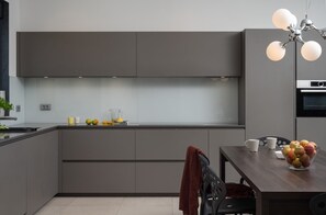 A modern kitchen with grey cabinetry, a dining table with chairs, and a fruit bowl.