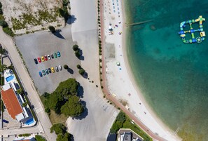 Vue aérienne d’une zone côtière comprenant un parking, une plage et une promenade en bord de mer.