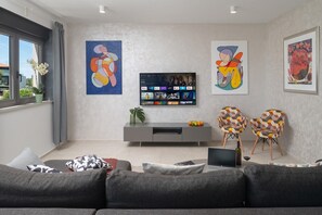 A modern living room with a grey sofa, a flat-screen TV, and abstract paintings on the walls.
