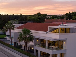 A modern two-story building with a flat roof, large windows, and a balcony with outdoor seating.