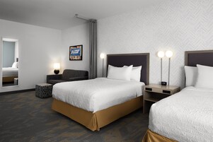 Una habitación de hotel con dos camas, una mesita de noche con un reloj, una lámpara en la mesita y un espejo en la pared.