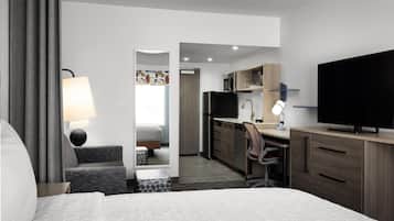 A hotel room with a bed, a desk, a chair, a television, and a bathroom visible through an open door.