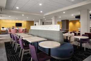 A modern restaurant with booths, round tables, and purple chairs.