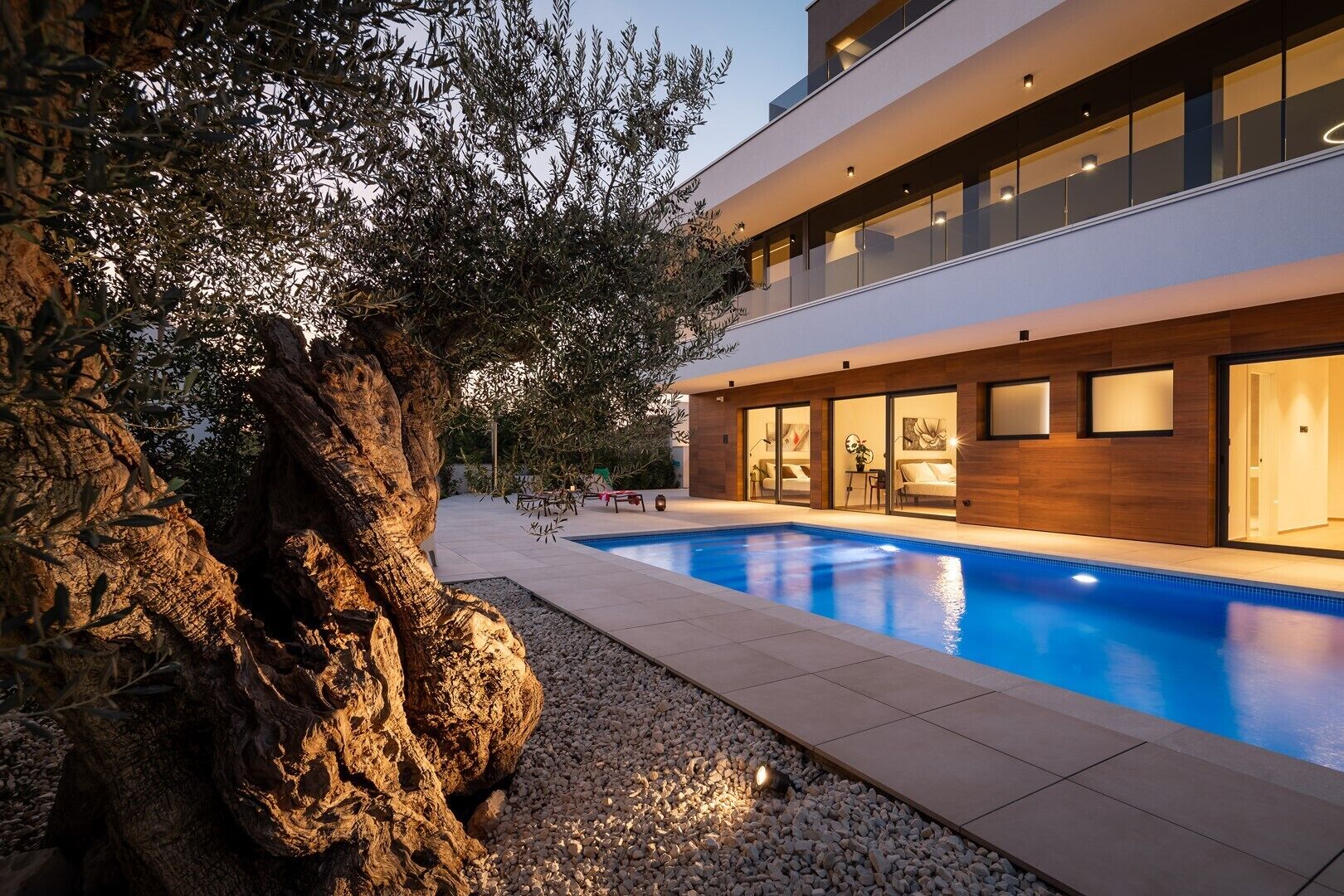 Un edificio moderno su due piani con piscina, area salotto esterna e un albero grande.