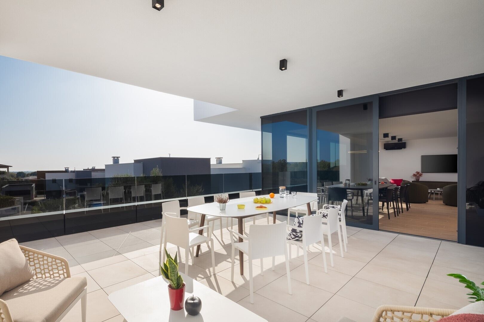 A modern outdoor dining area with a glass balustrade, white furniture, and a view of the cityscape.