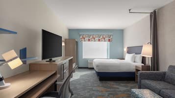 A hotel room with a bed, desk, TV, and seating area.