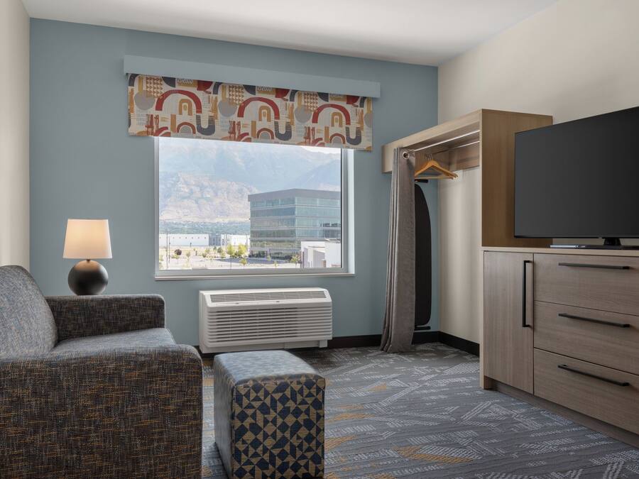 Habitación de hotel con sofá, televisión, ventana con vista a edificios y alfombra estampada.