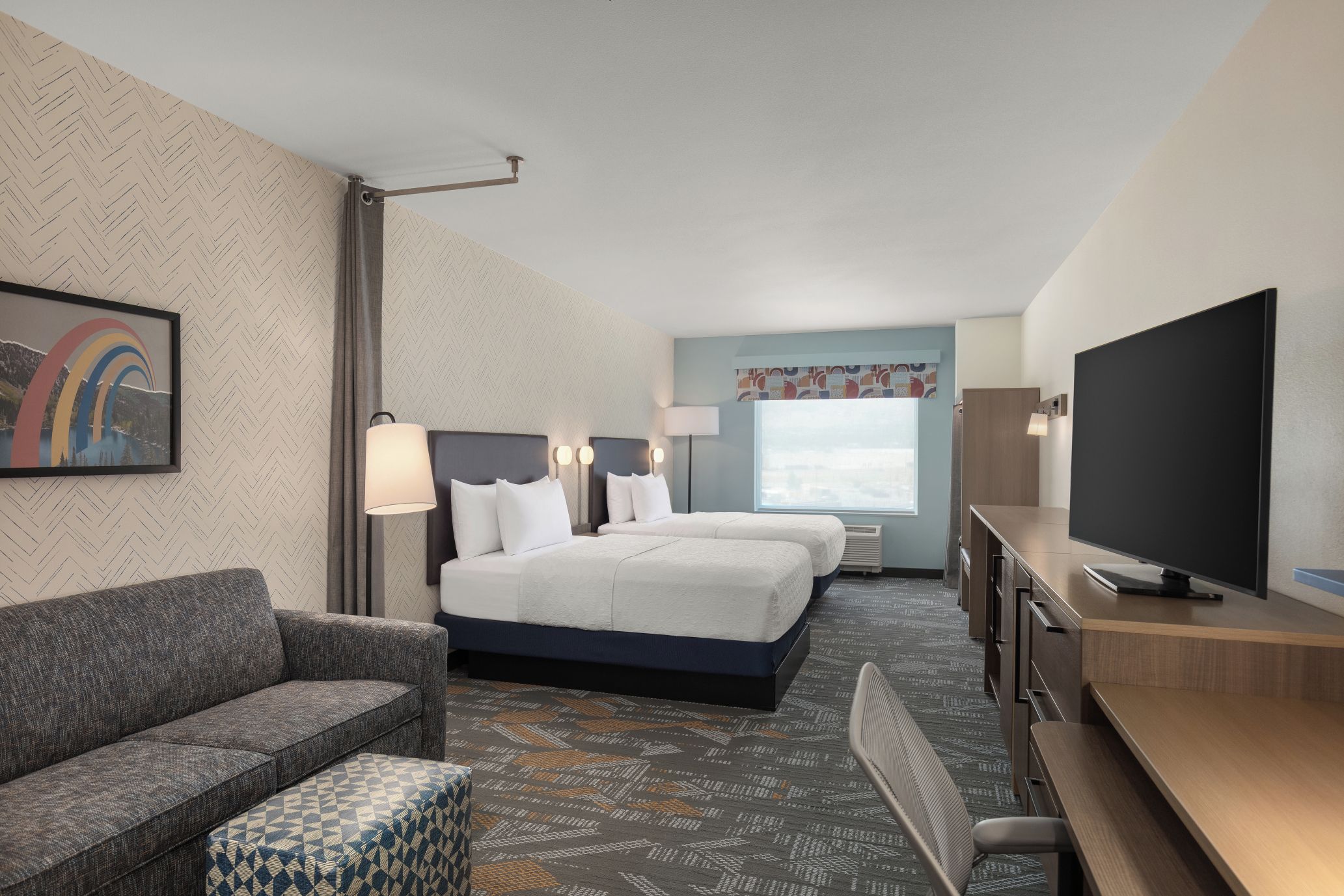 Habitación de hotel con cama, dos mesitas de noche, televisor, sofá y alfombra estampada.