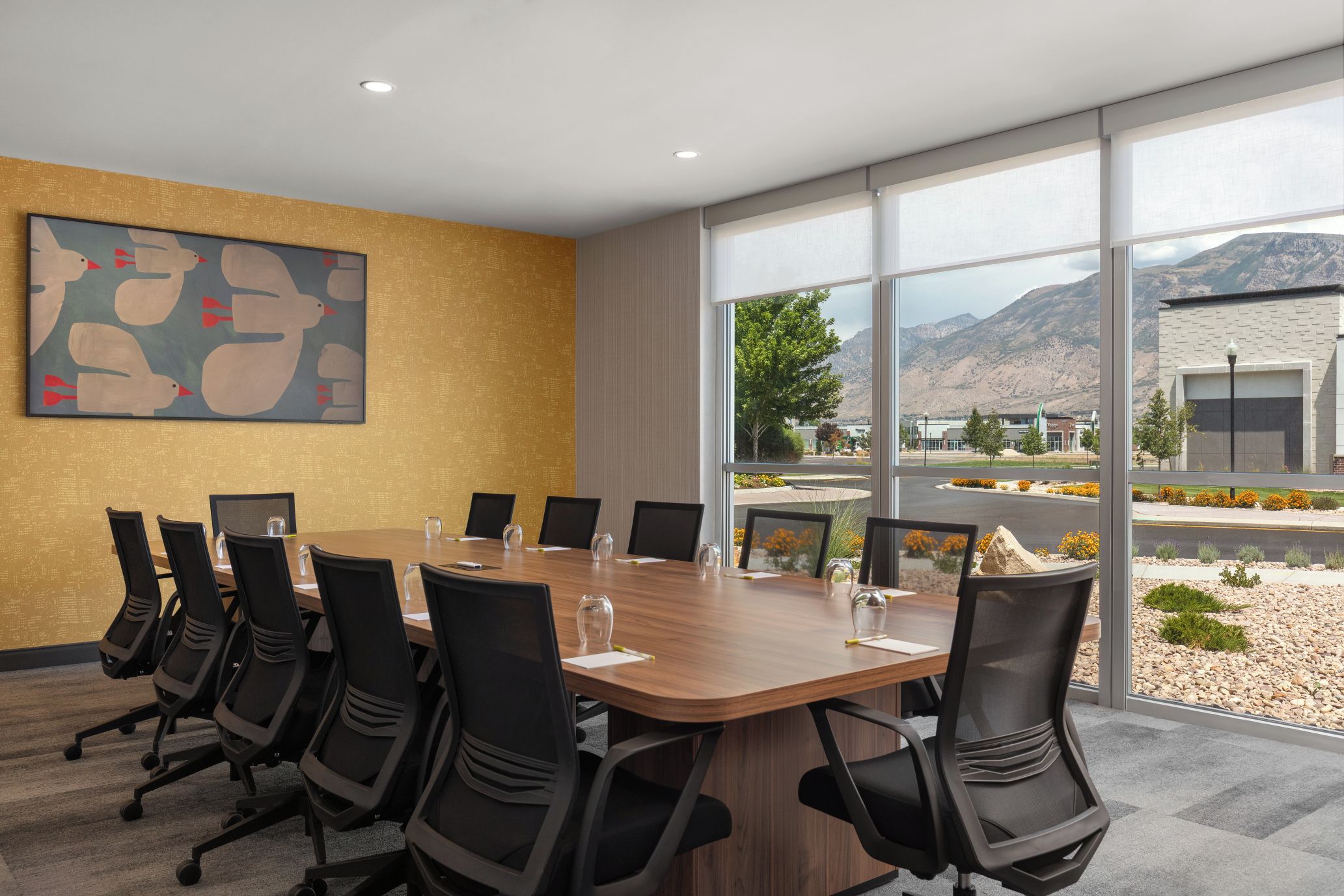 A conference room with a long table, chairs, and a large window with a mountain view.