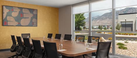 A conference room with a long table, chairs, and a large window with a mountain view.